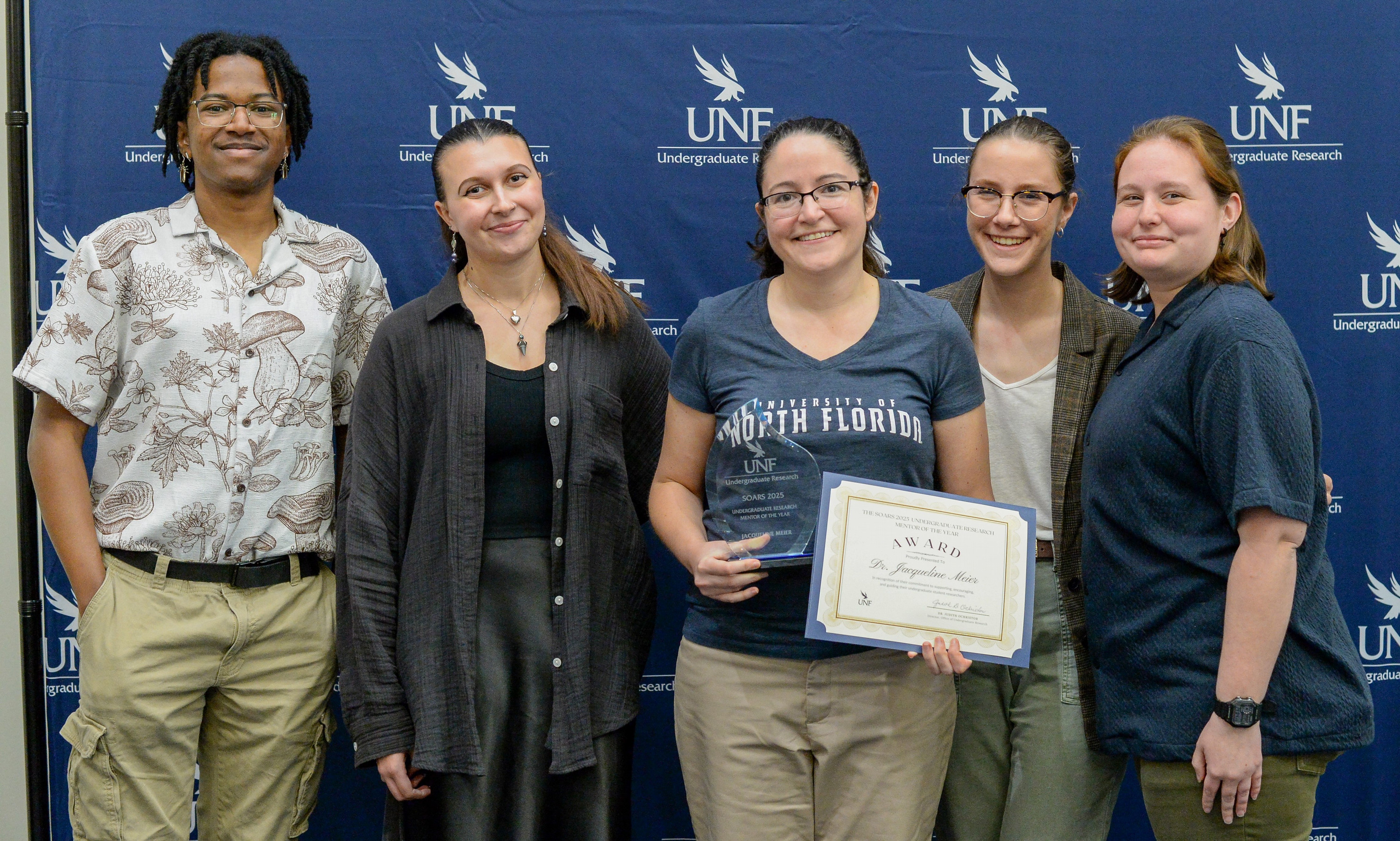 Jackie Meier standing and smiling with her students in front of a photo backdrop. 