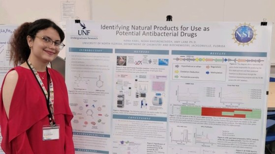 Hana wearing a red dress and standing in front of a research poster.