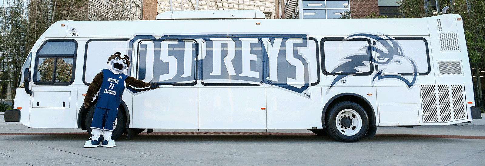 A parked Osprey Connector shuttle with Ozzie the mascot standing in front of the shuttle by the Student Union