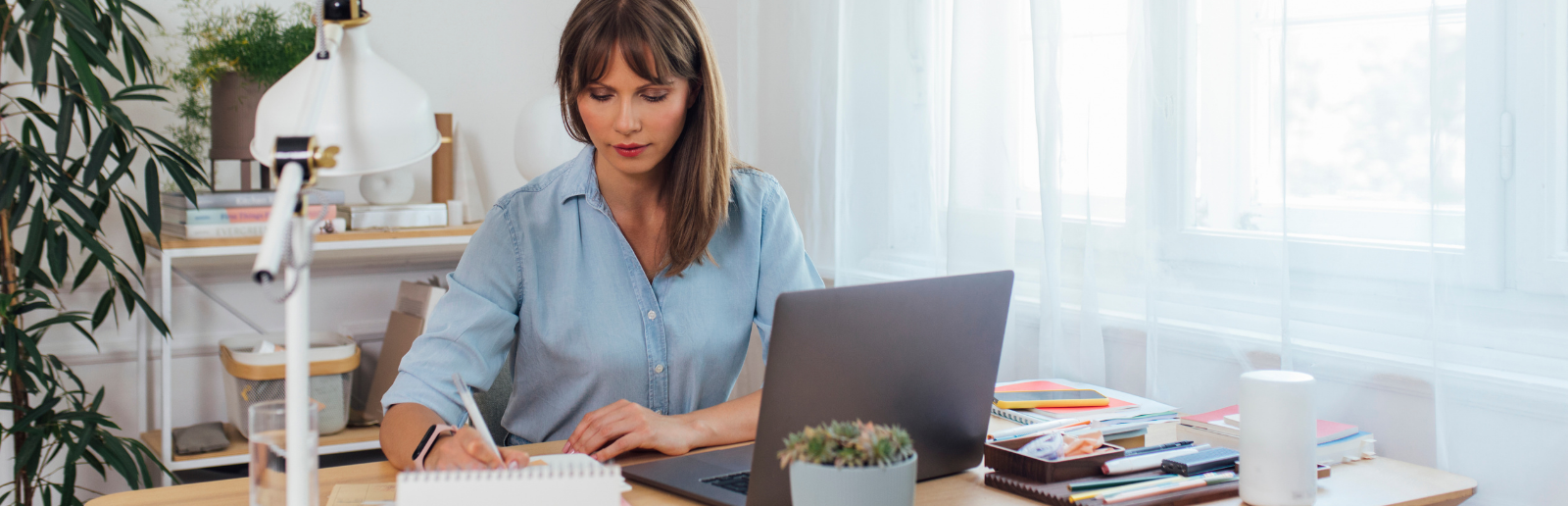 woman in blue business attire taking notes in front of the computer while she works