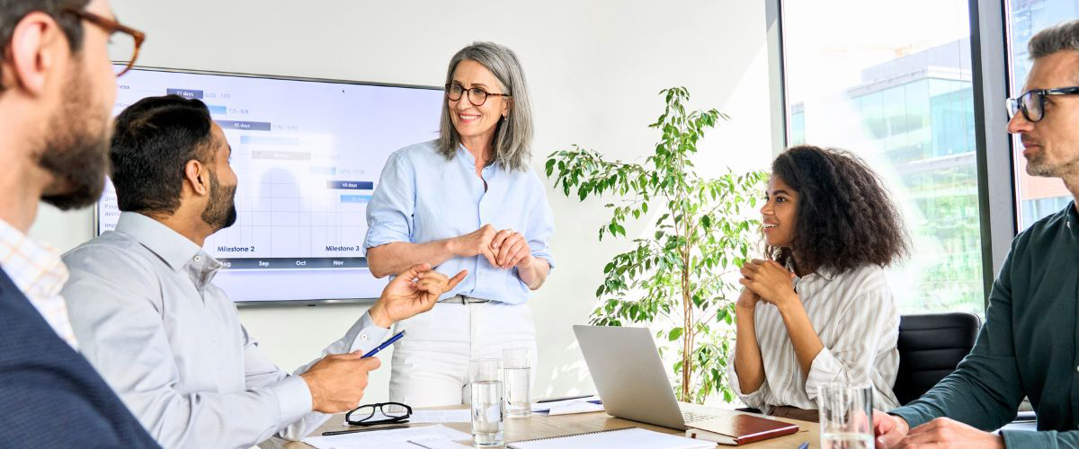 group of business professionals meeting together in conference room with a tv screen showing a calendar schedule