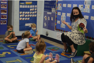 Teacher with students sitting around her while reading a book