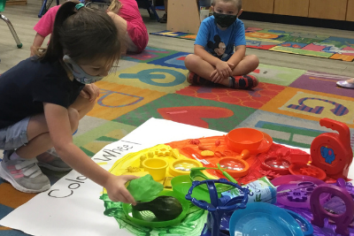 Students playing with rainbow colored toys on a color wheel