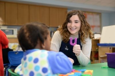 UNF staff member holding up the letter U while working with a preschooler