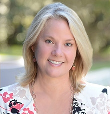 A smiling headshot of Vice President Heather Duncan. VP Duncan is wearing a floral top with white, black, and peach colors on it. 