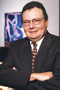 A smiling headshot with arms crossed of Interim President  Kline. Dr. Kline is wearing a black suit with a red and gold stripped tie. Dr. Kline is wearing glasses.
