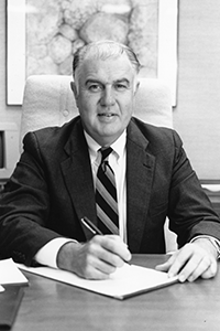 A black a white photo of interim president McTarnaghan while signing a piece of paper. 