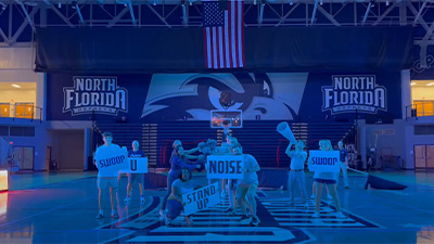 cheerleaders and athletics staff holding spirit signs in the gym