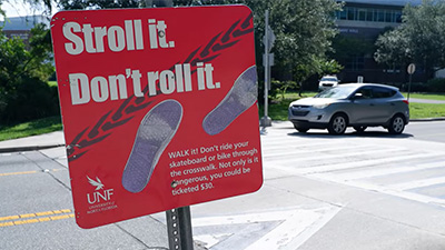 Cross walk with a sign in front of it that says stroll it. don't roll it.