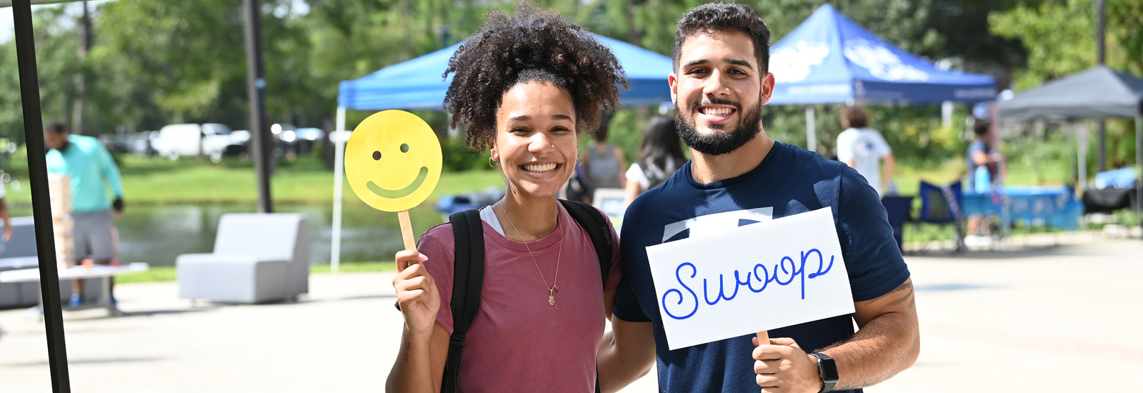 Male and female student outside in the student union courtyard holding up photo-booth signs and smiling