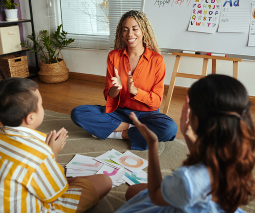 Female teacher sitting on the floor with her students clapping hands and smiling