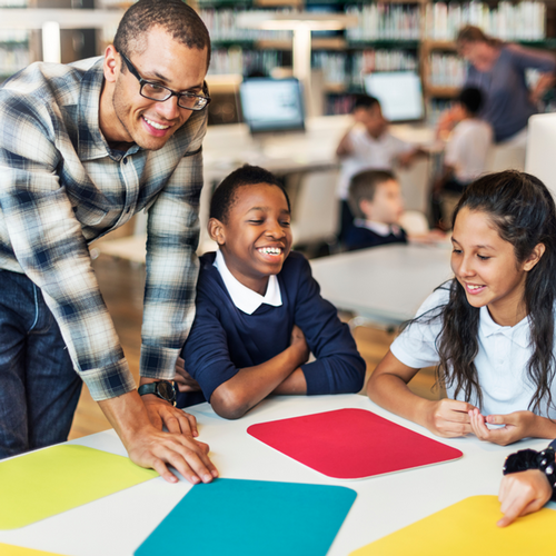 Male teacher with students smiling and looking at colorful pieces of paper