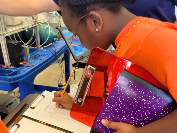 Elementary student in orange YMCA shirt in lab writing on clip board