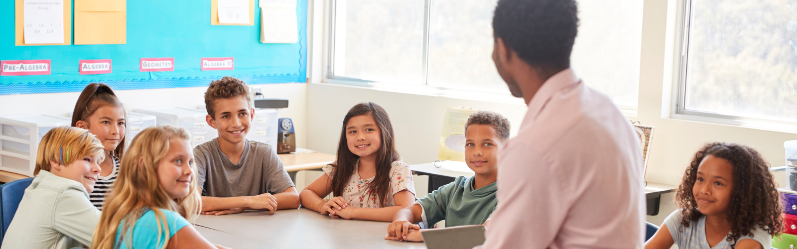 Teacher sits at a table with a group of students.