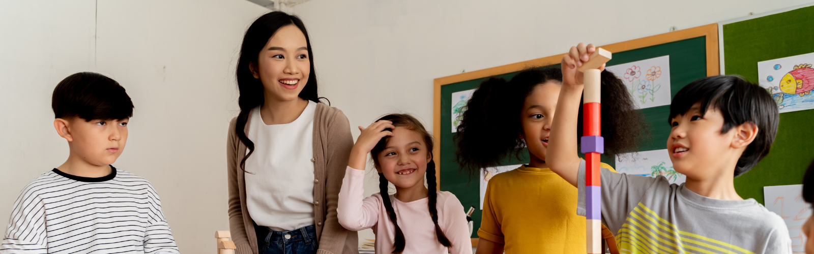 A teacher stands at a table with a group of student building block towers
