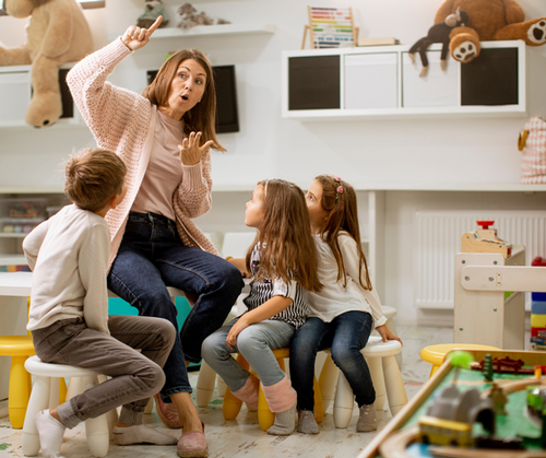 A teacher sits with a small group of students dramatically telling a story.