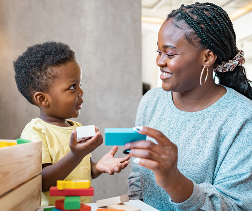 A young boy plays with blocks with his teacher.