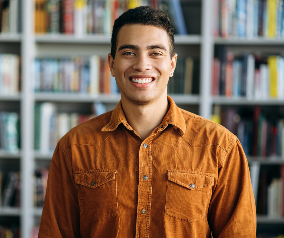 A teacher stands smiling in the library.
