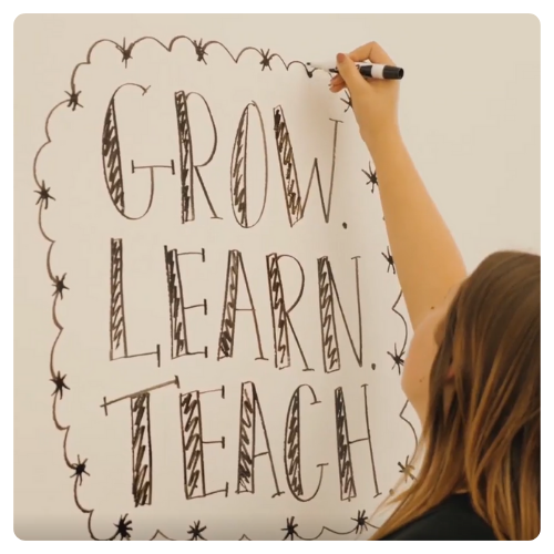 A teacher writing "Grow, learn, teach" on a white board