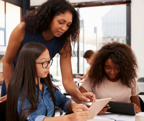 A teacher helps two students who are working on an ipad.