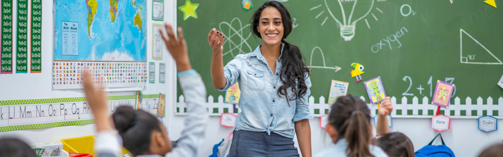 A teacher smiles while calling on students with their hands raised.