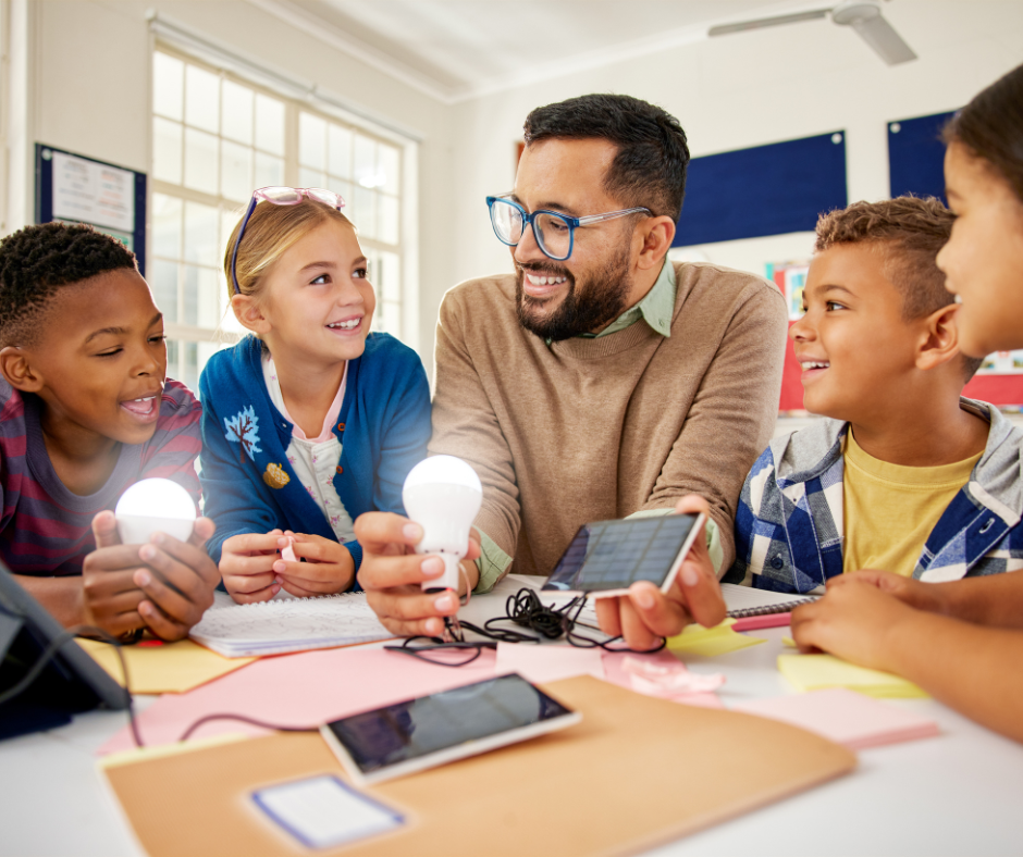 An elementary teacher sits with a group of students doing a science experiment