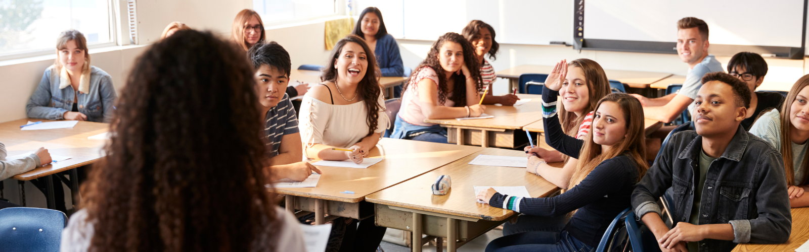 A Math teacher stands at the front of the classroom looking out at students at their desks. 