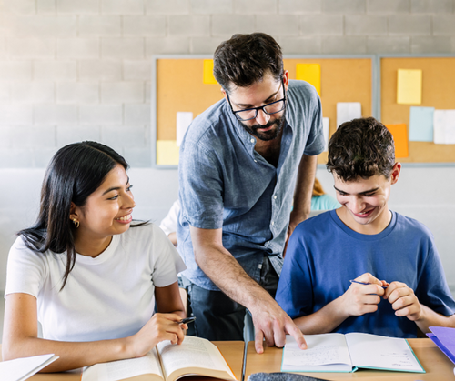 A teacher stands between two students and gives them feedback.