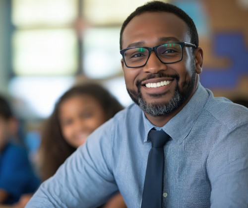 A teacher smiles while sitting in his classroom.
