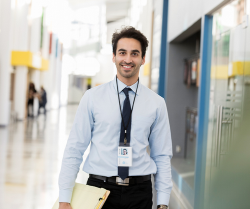 A high school teacher stands in a hallway smiling.