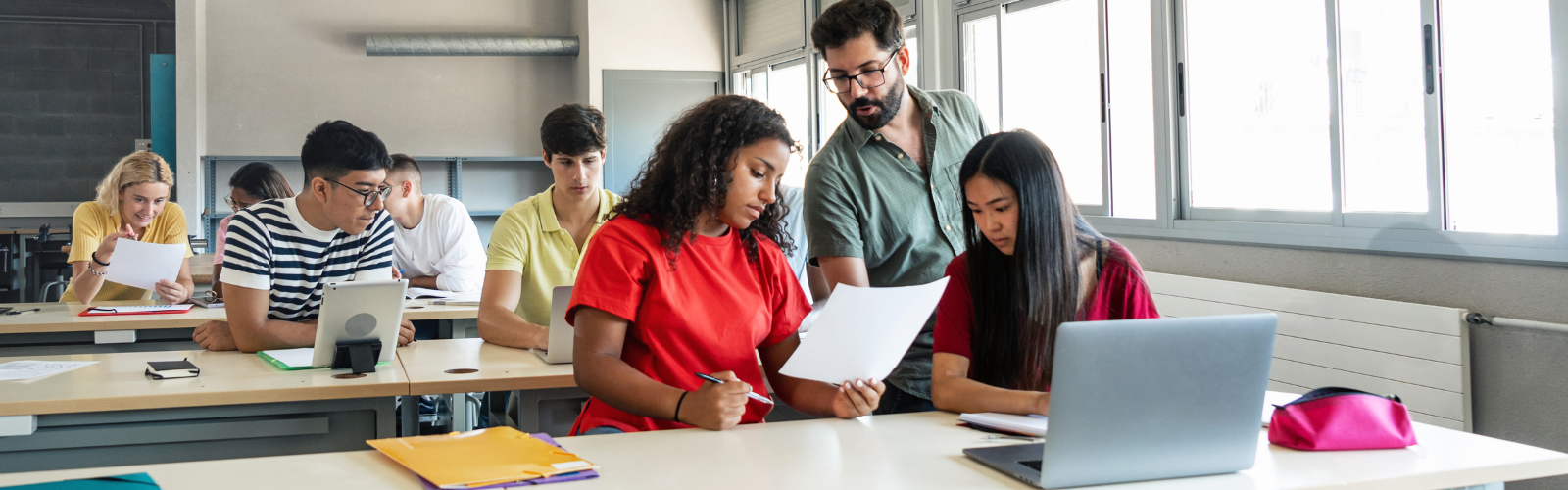A teacher gives two students feedback at their desk. 