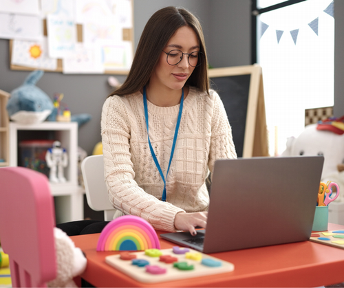 A teacher sits in her classroom working on her computer. 