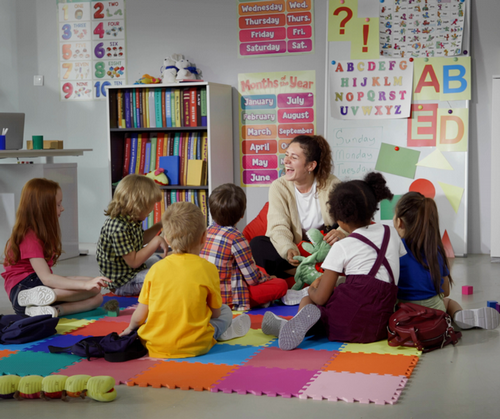 A teacher sits with a group of students in a primary grade classroom.