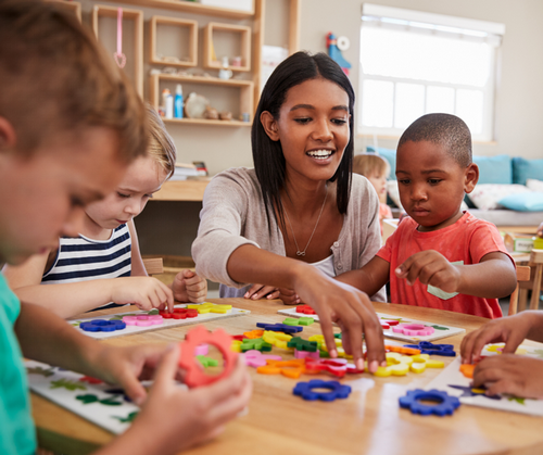 A preschool teacher helps a group of students complete a puzzle.