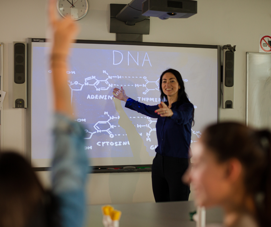 A high school biology teacher stands at the board with information about DNA structure.