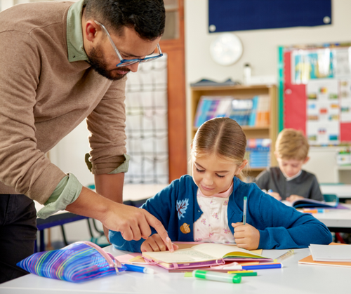 A teacher helps a student at their desk.