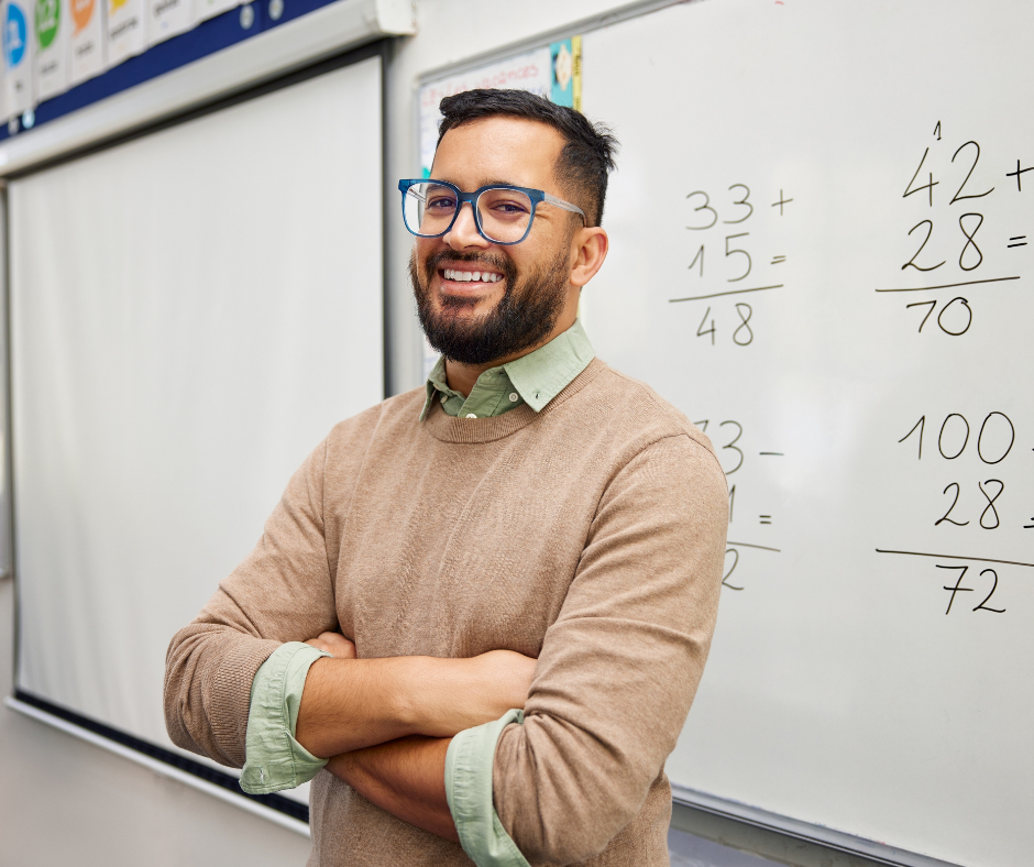 A math teacher stands in front of a whiteboard with work on it.