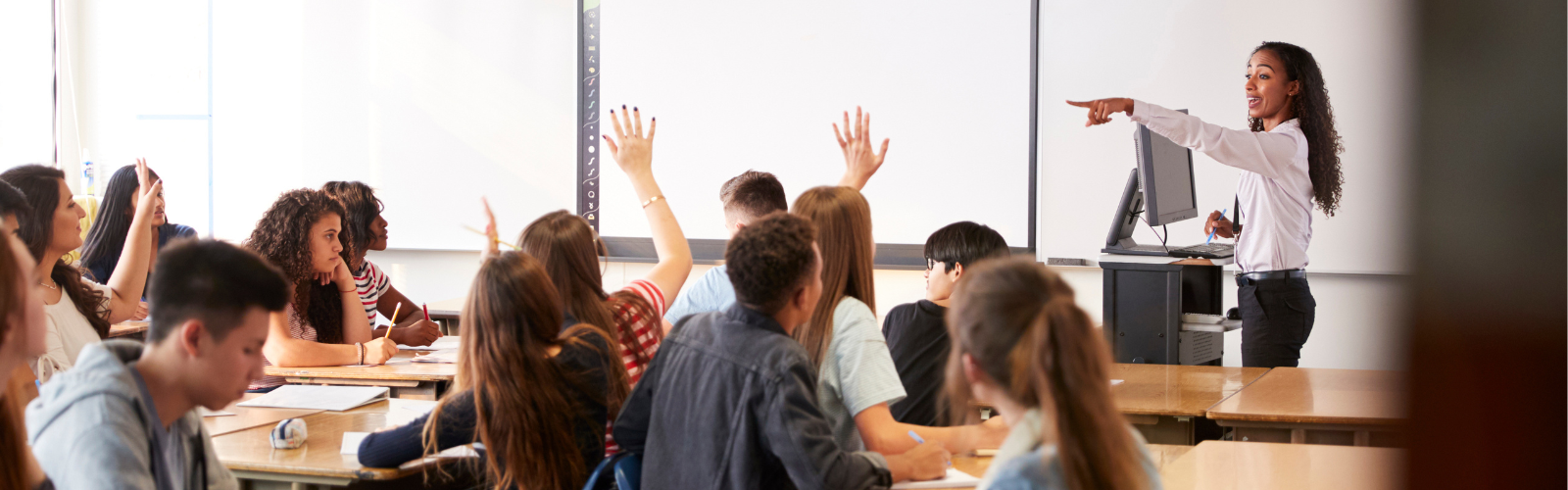 A high school Physics teacher calls on students with their hands raised in a classroom.