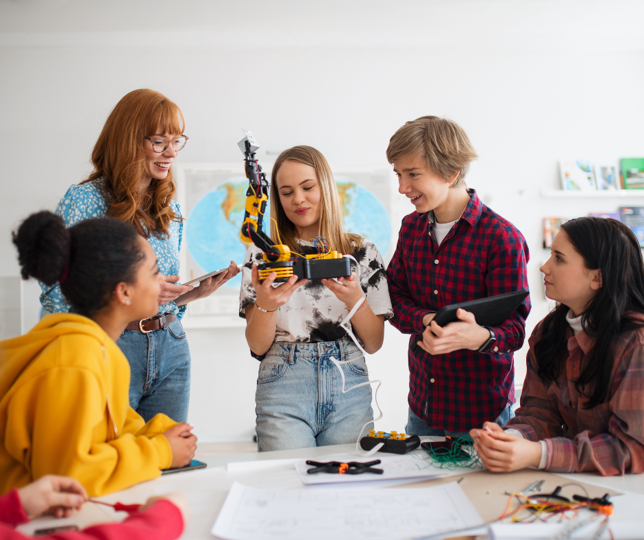 A science teacher stands with a group of students working with robotics.