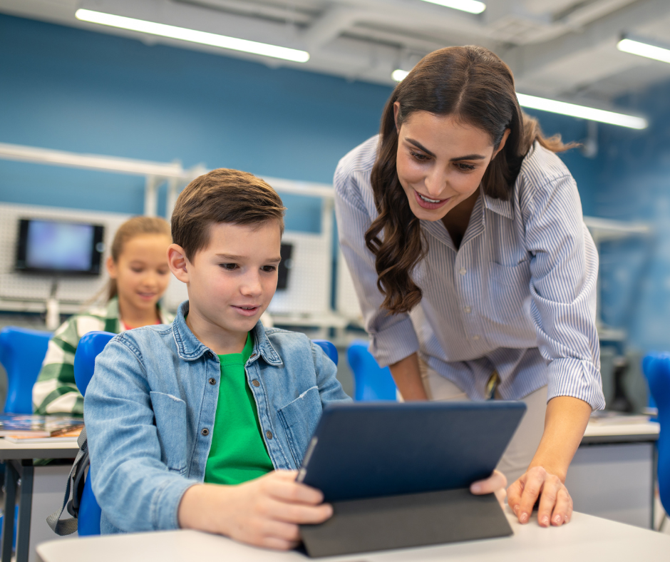 A teacher stands at a students desk and looks over their work.