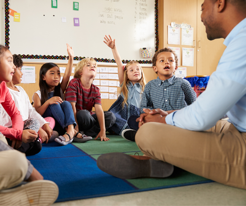 A teacher sits in a small group with students in a classroom.