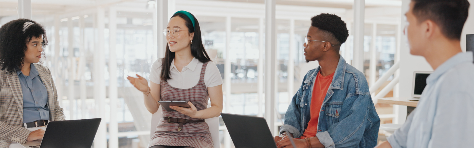 A group of four students talk to one another while working on iPads and laptops.