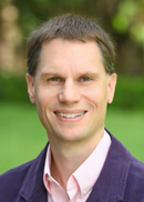 Headshot of Daniel Dinsmore in pink shirt and purple jacket