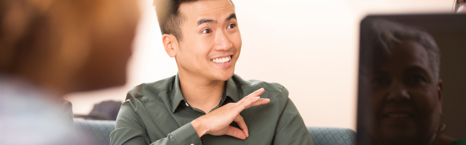 Asian man signing to other individuals in a meeting room.