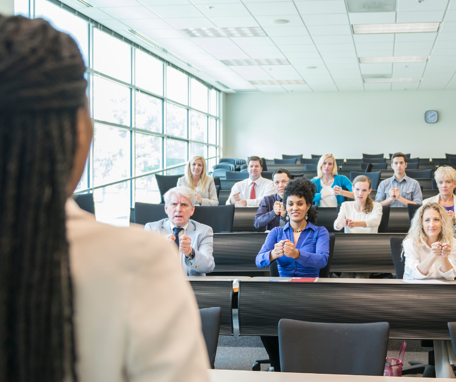 Woman stands in front of class learning ASL.