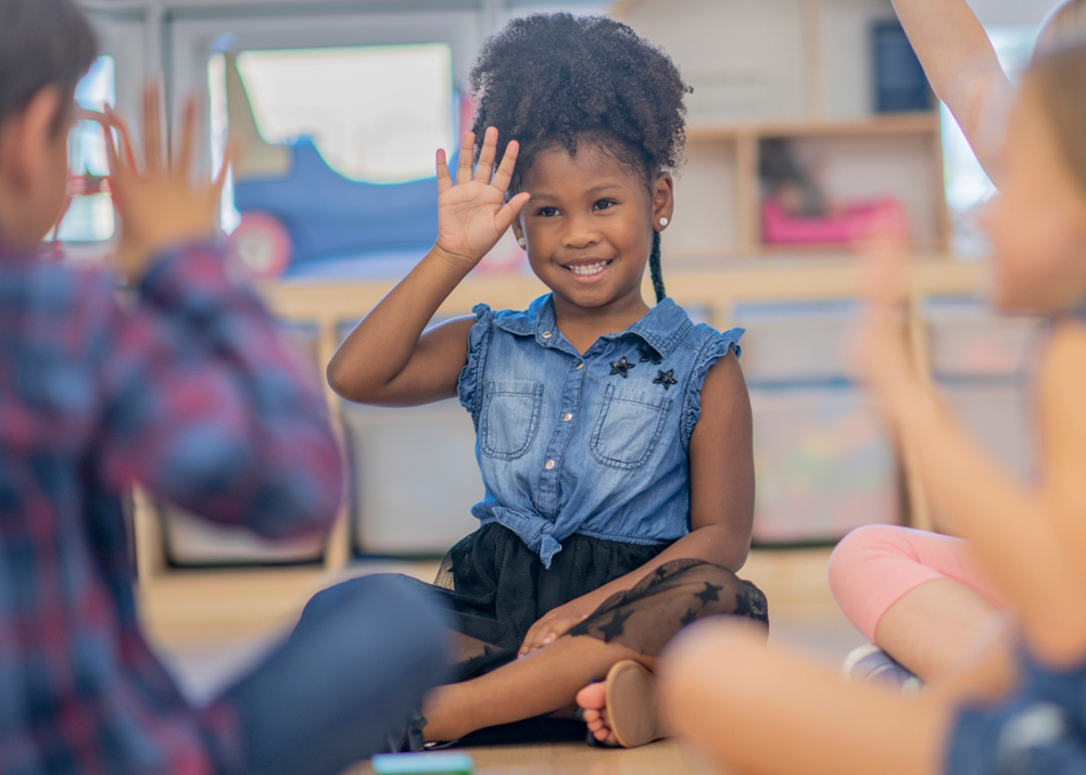 A young girl sitting in an elementary school setting using sign language