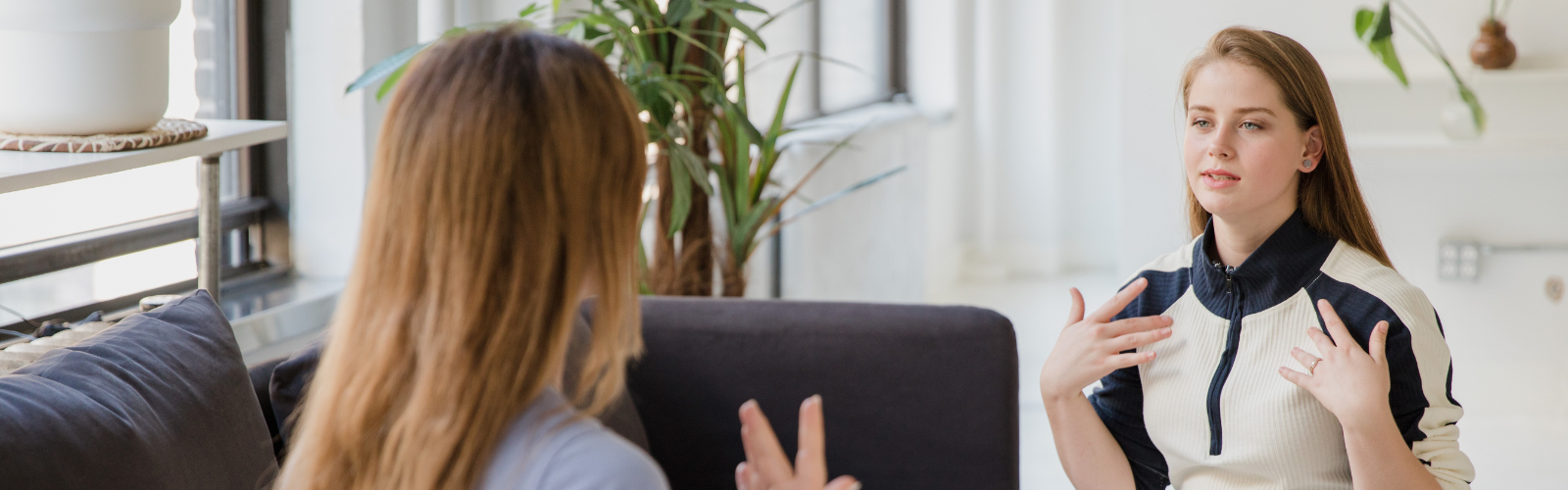 Two women sit on a couch communicating using ASL.