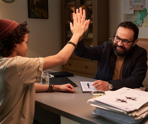 A school counselor high-fiving a young student in an office
