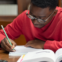 A man in a red sweatshirt taking down notes while studying