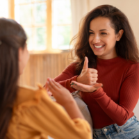 Two women communicate using ASL. One is smiling, the other's back is turned.